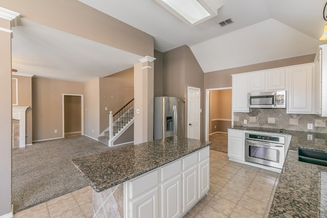 kitchen with stainless steel appliances, dark stone counters, white cabinets, light carpet, and tasteful backsplash