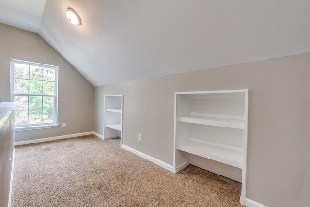 bonus room with built in shelves, light colored carpet, and lofted ceiling