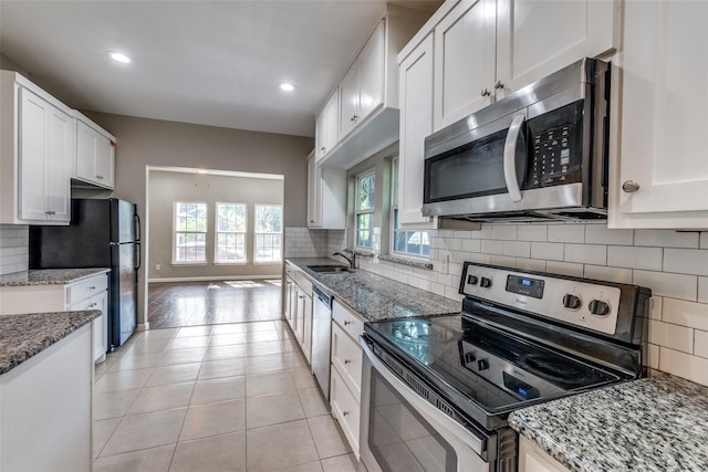 kitchen with tasteful backsplash, light stone counters, stainless steel appliances, light tile patterned floors, and white cabinets