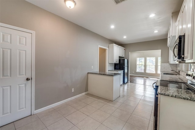 kitchen with white cabinets, appliances with stainless steel finishes, light tile patterned floors, and dark stone countertops