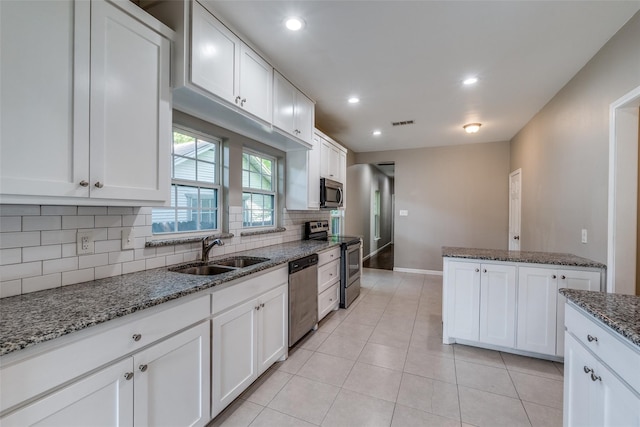 kitchen with sink, appliances with stainless steel finishes, dark stone counters, white cabinets, and decorative backsplash