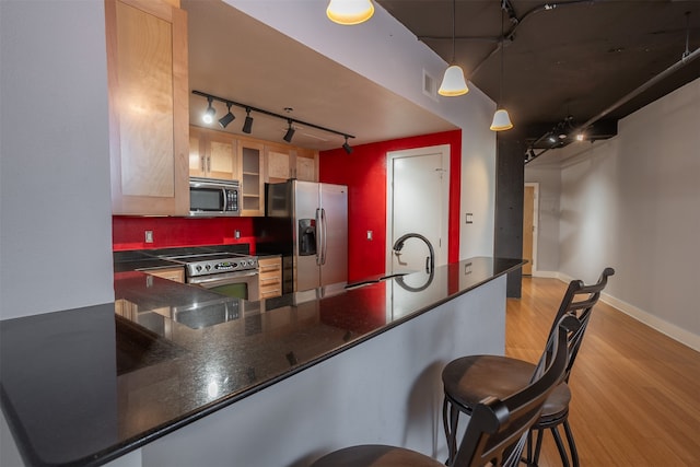 kitchen with stainless steel appliances, sink, kitchen peninsula, a kitchen bar, and light hardwood / wood-style flooring