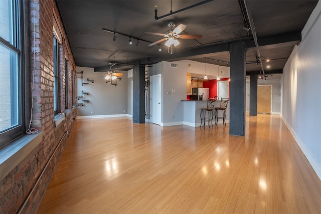 unfurnished living room featuring brick wall, light wood-type flooring, and rail lighting