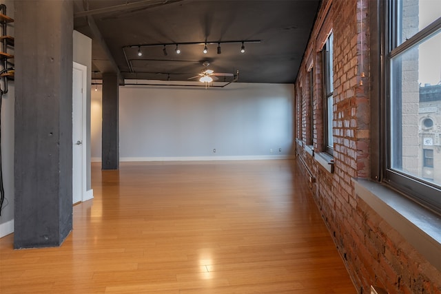 unfurnished living room featuring ceiling fan, brick wall, light wood-type flooring, and track lighting