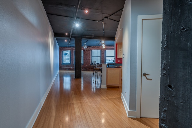 corridor featuring light wood-type flooring, sink, and brick wall