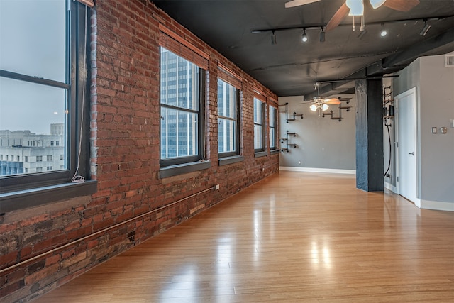 unfurnished room with light hardwood / wood-style floors, rail lighting, and brick wall