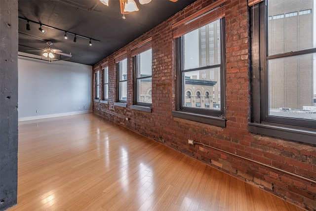 empty room featuring light hardwood / wood-style floors, ceiling fan, rail lighting, and brick wall