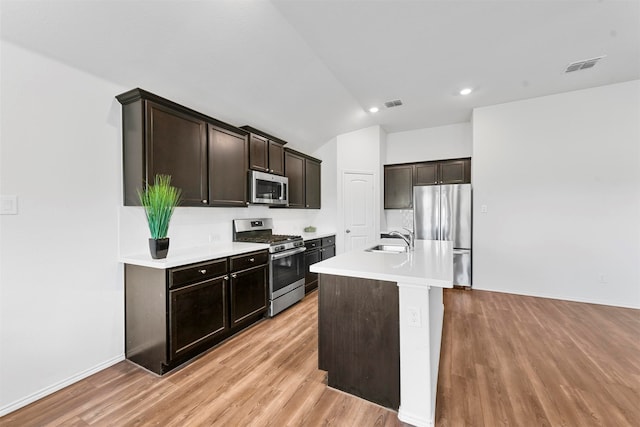 kitchen featuring dark brown cabinetry, sink, an island with sink, appliances with stainless steel finishes, and light wood-type flooring