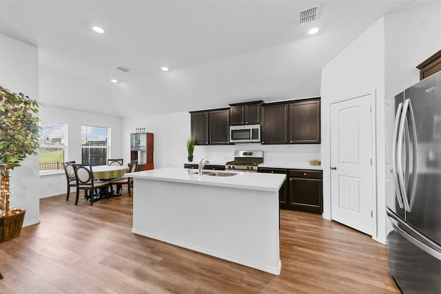 kitchen featuring light wood-type flooring, dark brown cabinets, stainless steel appliances, sink, and an island with sink