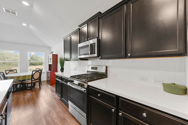 kitchen featuring appliances with stainless steel finishes, backsplash, dark hardwood / wood-style flooring, dark brown cabinetry, and lofted ceiling