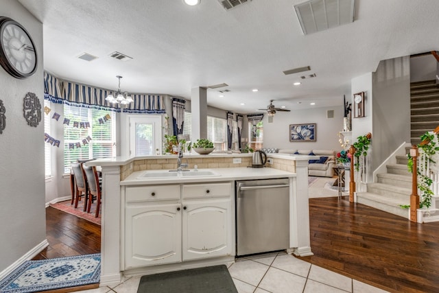 kitchen featuring hanging light fixtures, sink, stainless steel dishwasher, light tile patterned floors, and white cabinetry