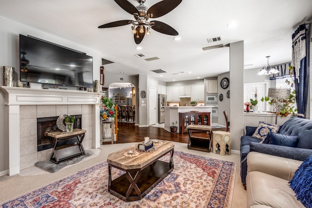 living room with a tile fireplace and ceiling fan with notable chandelier