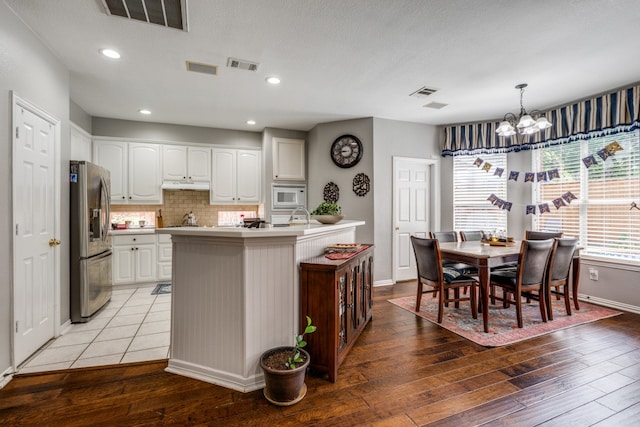 kitchen with stainless steel refrigerator with ice dispenser, white microwave, wood-type flooring, decorative light fixtures, and white cabinets