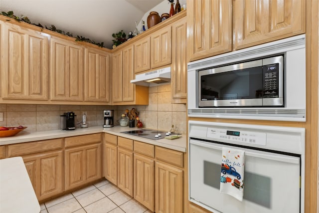 kitchen featuring black electric stovetop, stainless steel microwave, light tile patterned floors, white oven, and light brown cabinetry