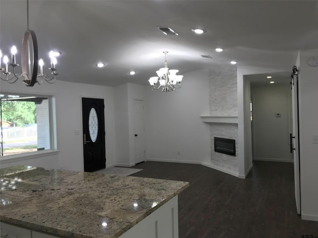 kitchen featuring white cabinetry, light stone countertops, decorative light fixtures, a fireplace, and dark hardwood / wood-style flooring