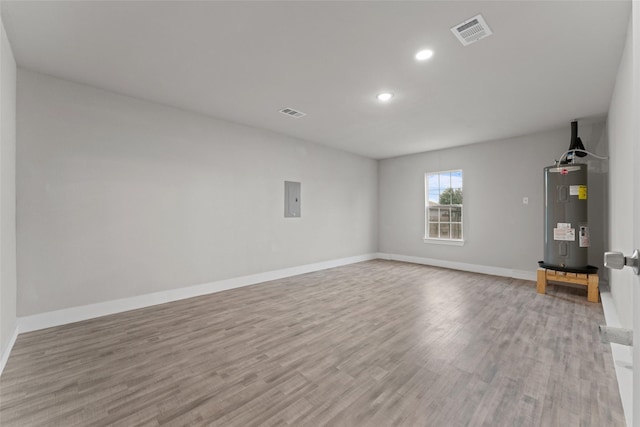 empty room with electric panel, electric water heater, and light wood-type flooring