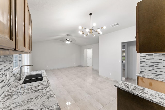 kitchen with vaulted ceiling, sink, backsplash, light stone counters, and ceiling fan with notable chandelier