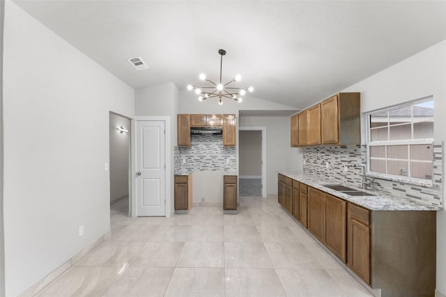 kitchen featuring pendant lighting, vaulted ceiling, sink, light stone counters, and an inviting chandelier