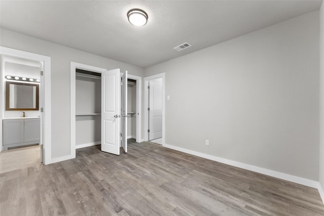 unfurnished bedroom with sink, connected bathroom, light hardwood / wood-style flooring, and a textured ceiling