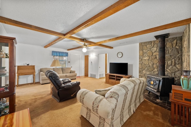 living room featuring a textured ceiling, a wood stove, beamed ceiling, ceiling fan, and carpet