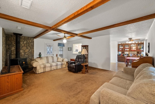 carpeted living room with ceiling fan, a wood stove, a textured ceiling, and beam ceiling