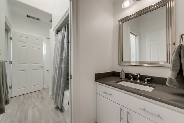 bathroom with hardwood / wood-style flooring, vanity, and shower / bathtub combination with curtain