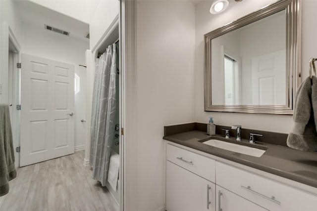 bathroom with wood finished floors, vanity, shower / bath combo with shower curtain, and baseboards