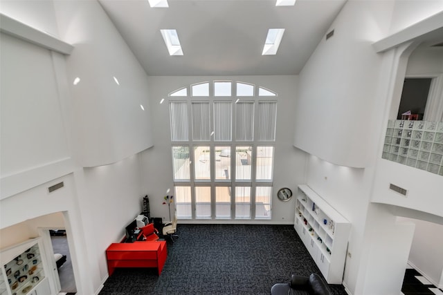 carpeted living room with high vaulted ceiling, a skylight, and baseboards