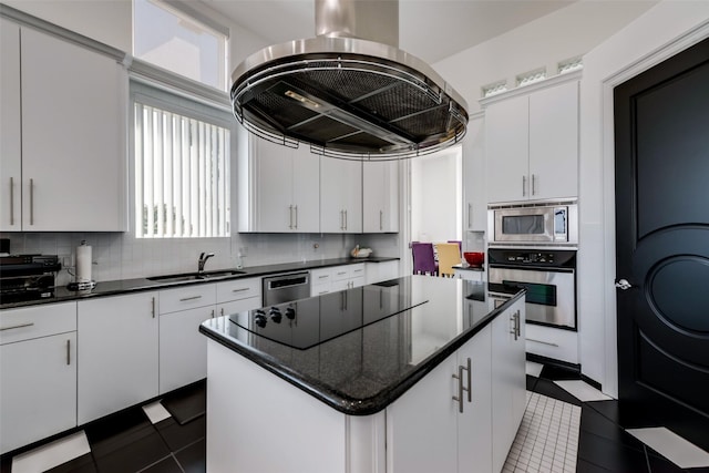 kitchen with stainless steel appliances, a sink, island exhaust hood, dark tile patterned flooring, and white cabinetry