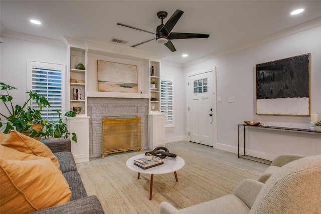 living room featuring built in shelves, ceiling fan, crown molding, light hardwood / wood-style floors, and a fireplace