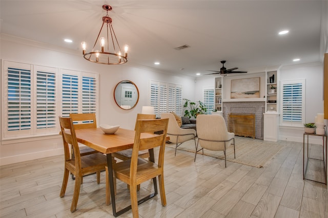 dining space with a fireplace, light wood-type flooring, and ceiling fan with notable chandelier