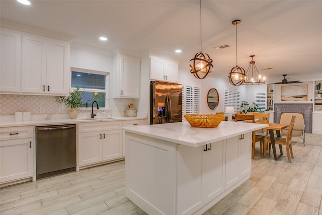 kitchen featuring white cabinetry, sink, hanging light fixtures, stainless steel appliances, and a kitchen island