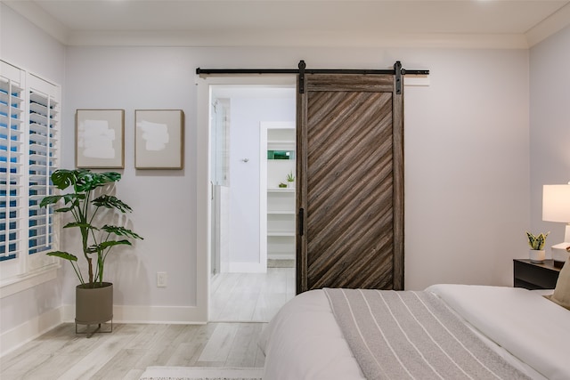 bedroom featuring a barn door, crown molding, and light hardwood / wood-style flooring