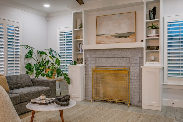 living room with a brick fireplace, ornamental molding, and light hardwood / wood-style flooring