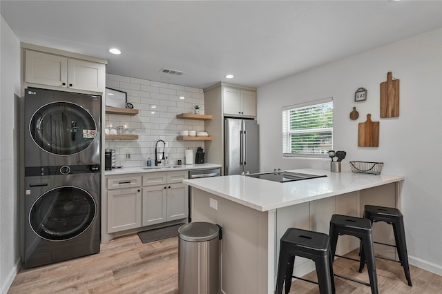 kitchen featuring a kitchen bar, stainless steel appliances, light hardwood / wood-style floors, kitchen peninsula, and stacked washer / dryer