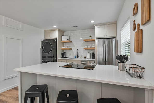 kitchen featuring stacked washer and clothes dryer, tasteful backsplash, a breakfast bar, light wood-type flooring, and appliances with stainless steel finishes