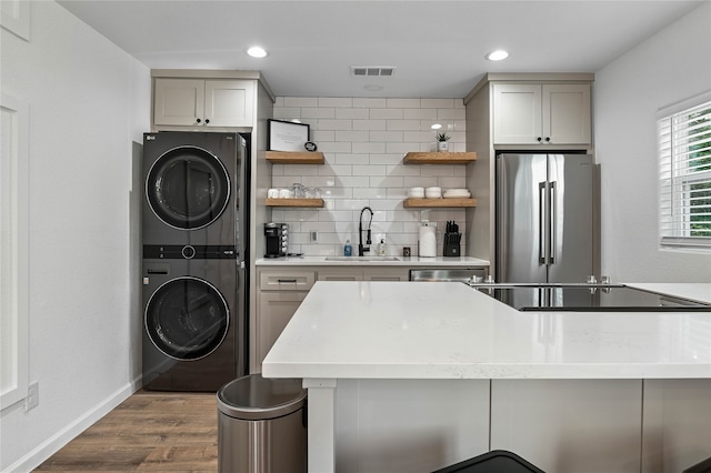 kitchen with stacked washing maching and dryer, a kitchen bar, stainless steel refrigerator, hardwood / wood-style floors, and sink