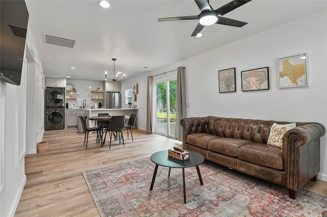 living room featuring stacked washing maching and dryer, ceiling fan with notable chandelier, sink, and light wood-type flooring