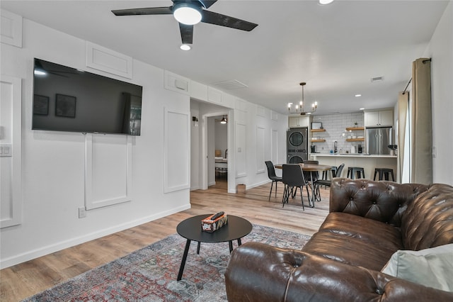 living room with stacked washer / dryer, light wood-type flooring, sink, and ceiling fan with notable chandelier