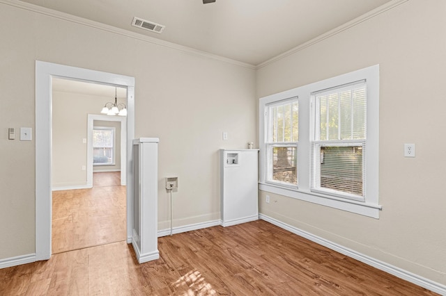 spare room with plenty of natural light, hardwood / wood-style flooring, crown molding, and an inviting chandelier