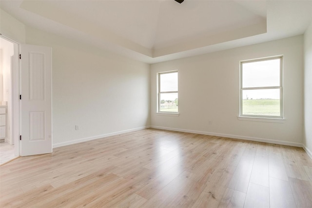 unfurnished room with light wood-type flooring and a tray ceiling