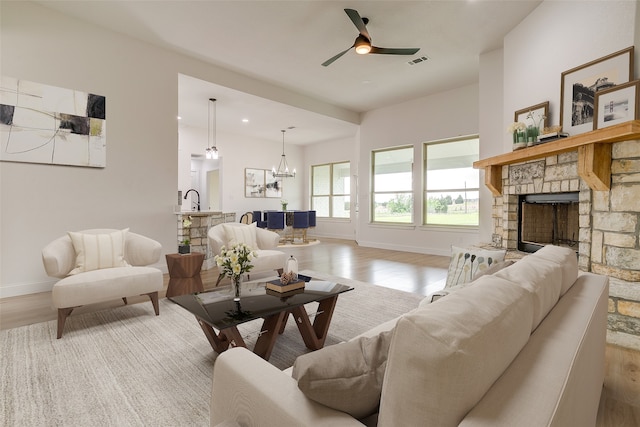 living room with a fireplace, ceiling fan with notable chandelier, light hardwood / wood-style flooring, and sink