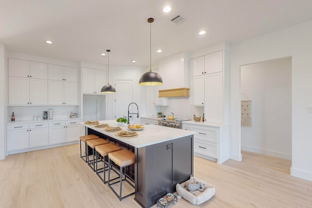 kitchen featuring an island with sink, light hardwood / wood-style floors, white cabinetry, and decorative light fixtures