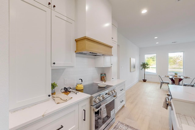 kitchen with light hardwood / wood-style floors, high end stainless steel range oven, white cabinets, tasteful backsplash, and custom exhaust hood