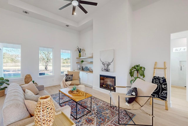 living room with a high ceiling, ceiling fan, and light hardwood / wood-style floors