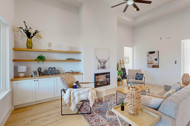 living room featuring light wood-type flooring, ceiling fan, and a high ceiling