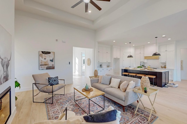 living room featuring ceiling fan, light hardwood / wood-style floors, and a towering ceiling