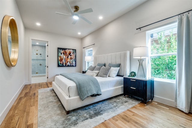 bedroom with ensuite bathroom, ceiling fan, multiple windows, and light wood-type flooring