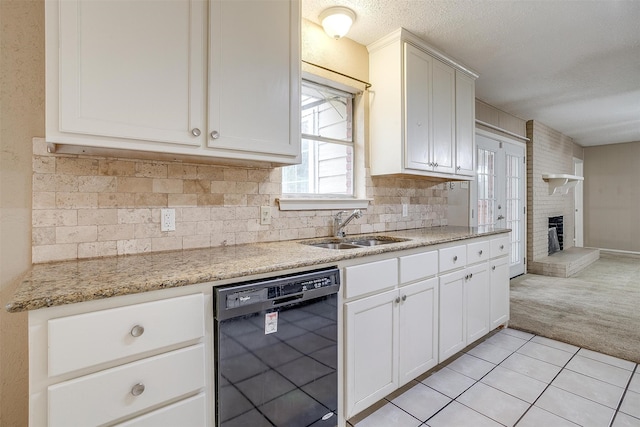 kitchen featuring black dishwasher, a brick fireplace, sink, and white cabinets