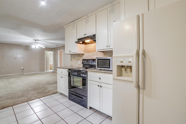 kitchen featuring black electric range, wooden walls, tasteful backsplash, white refrigerator with ice dispenser, and light tile patterned flooring